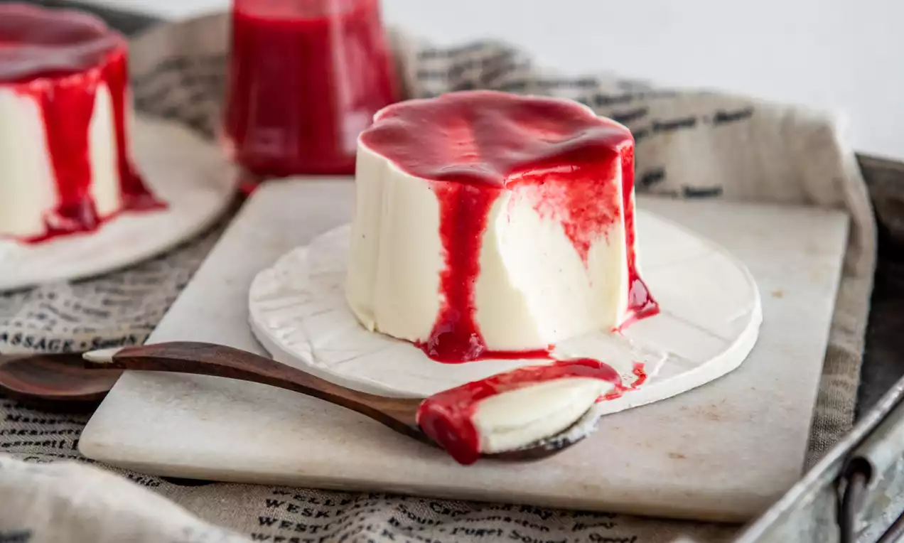 Picture - Panna cotta color avorio dalla superficie liscia, coperta da una colata lucida di salsa rosso brillante su un piattino bianco