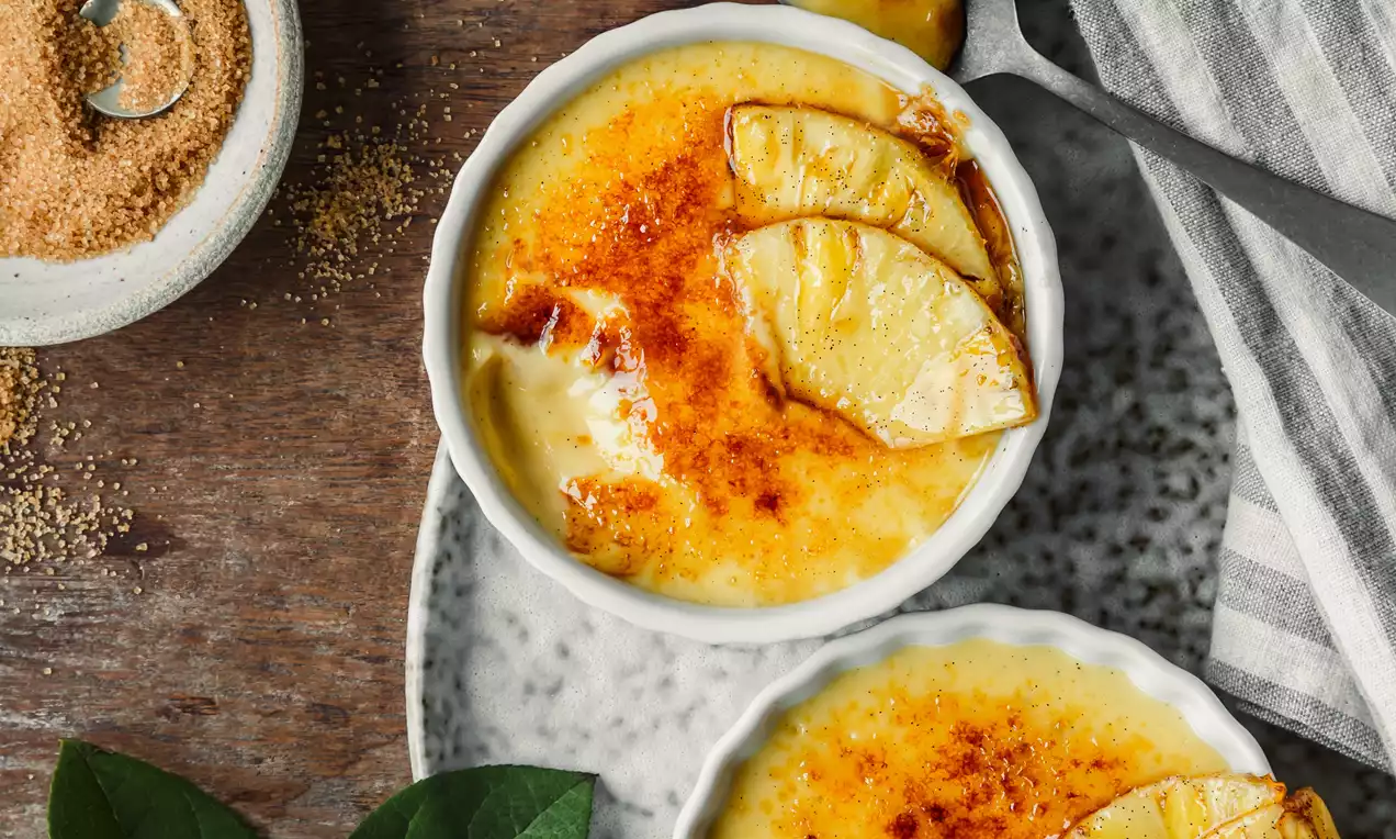 Picture - Cremosi strati giallo chiaro con crosta caramellata dorata, decorati con fettine di ananas su piatti marmorizzati accanto a zucchero e vaniglia